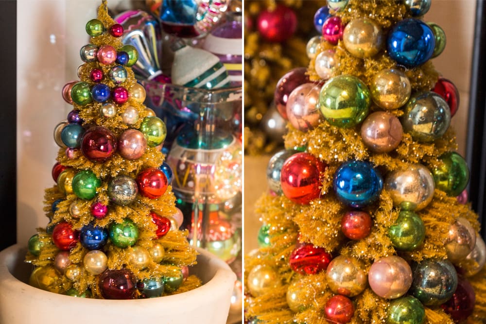 Yellow colored bottle brush tree with brightly colored glass ornaments adhered to the tree resting in a mortar.