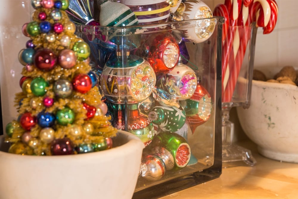 Mortar filled with yellow bottle brush tree with glass ornaments with glass block filled with glass vintage ornaments.