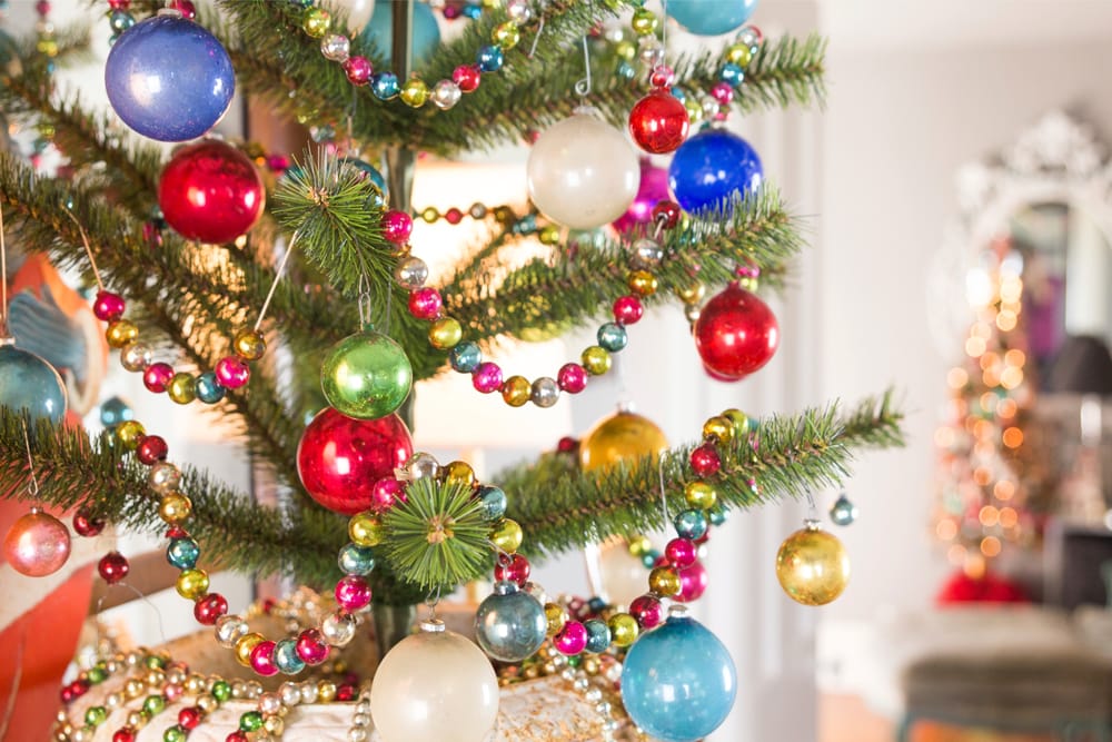 Christmas tree with beads of garland made from glass with lots of colored glass ornaments all over tree.