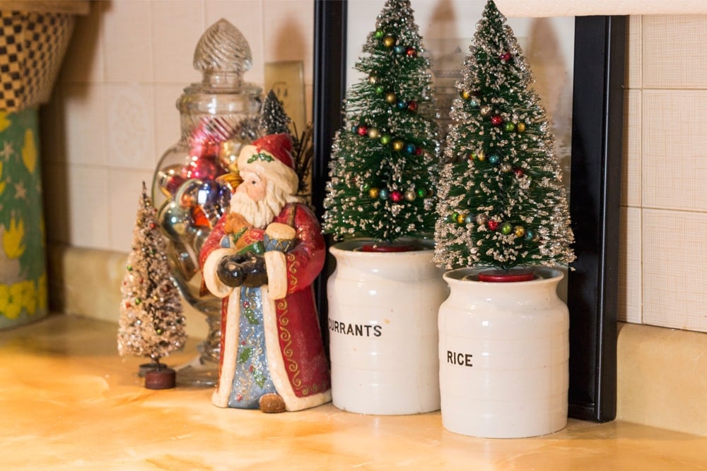 Kitchen jars with Santa to the side with bottle brush trees on top with glass jar filled with ornaments.