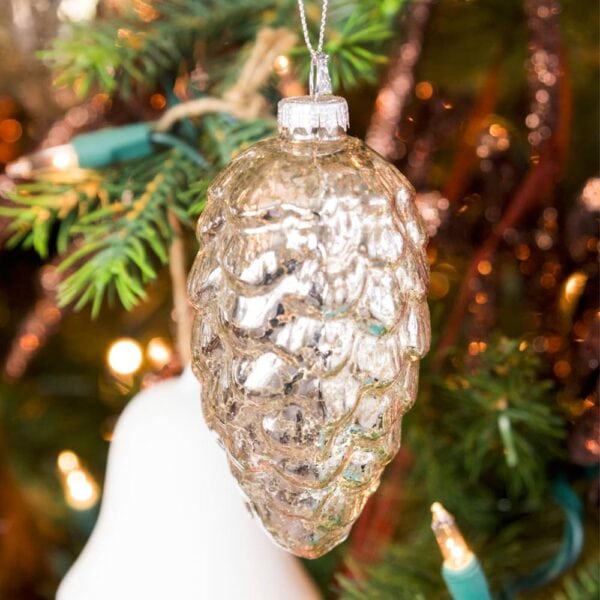 Glass silver mushroom ornament hanging from a bough of a Christmas tree with white bell in the background.