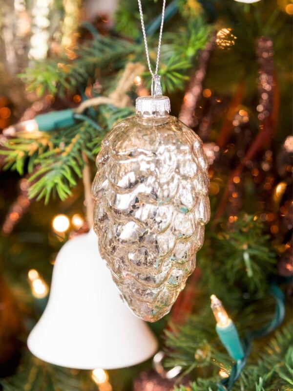 Glass silver mushroom ornament hanging from a bough of a Christmas tree with white bell in the background.