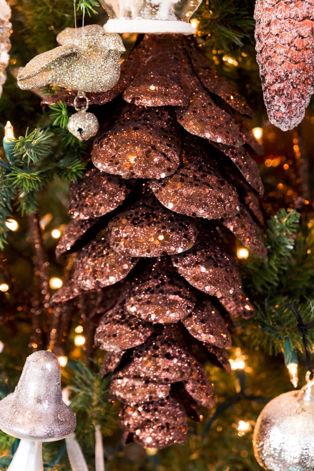 Brown sparkly mushroom ornament hanging on a Christmas tree with more ornaments all around.
