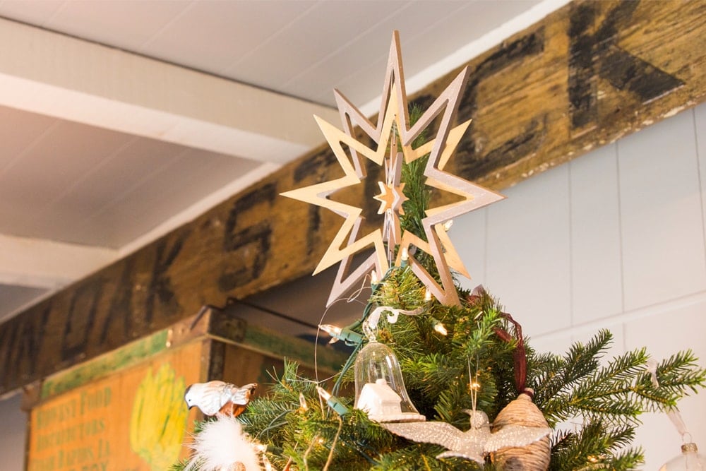 Wooden star placed on top of a Christmas tree filled with mushroom ornaments with old store sign in background.