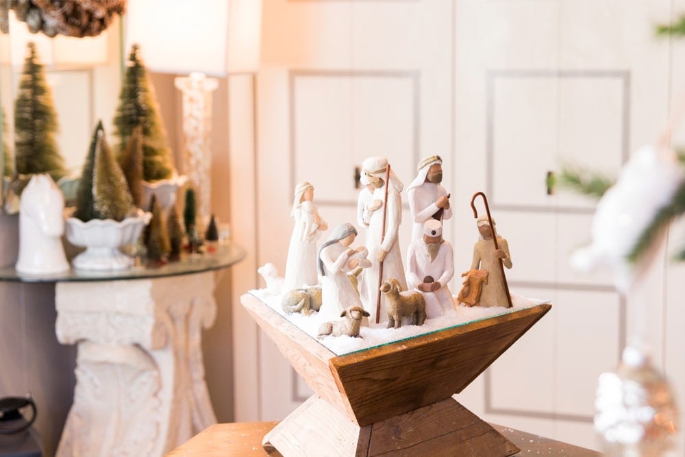 Nativity scene with shepherds and wise men sitting on a wooden block on table with trees in background.