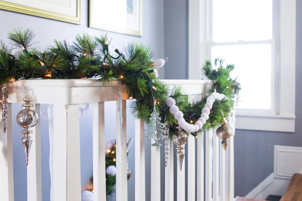White banister and railing adorned with evergreen garland and white balls with silver ornaments.