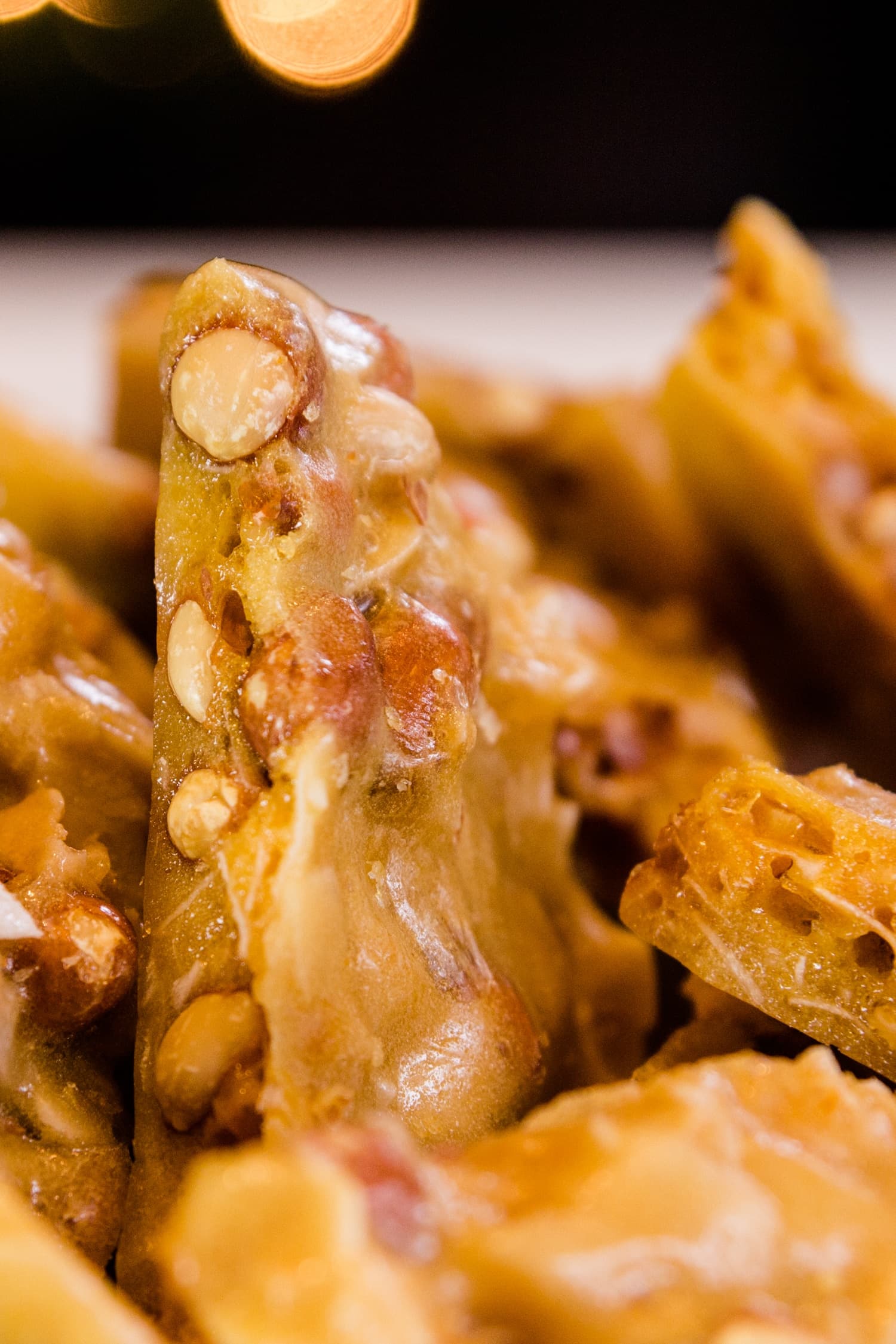 Golden peco candy with peanuts and flakes of coconut piled high on a white surface with Christmas lights in background