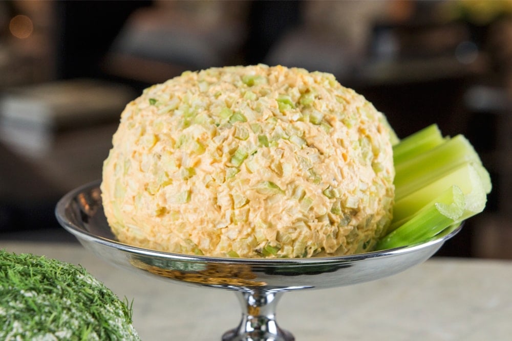 Buffalo blue cheese ball sitting on metal serving bowl with slices of celery