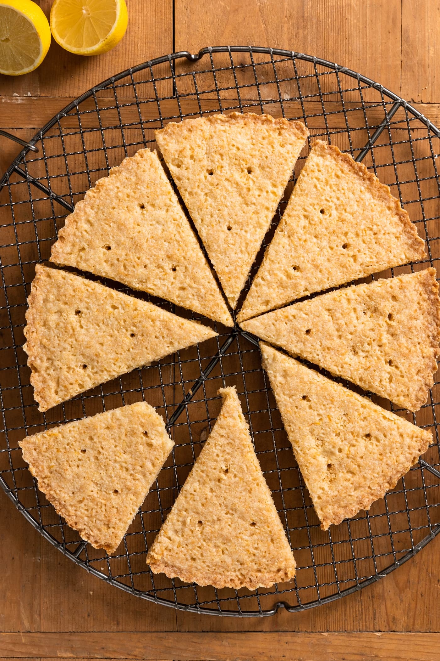 Top down view of triangle-shaped lemon shortbread cookies sitting on wire cooling rack all on wood surface