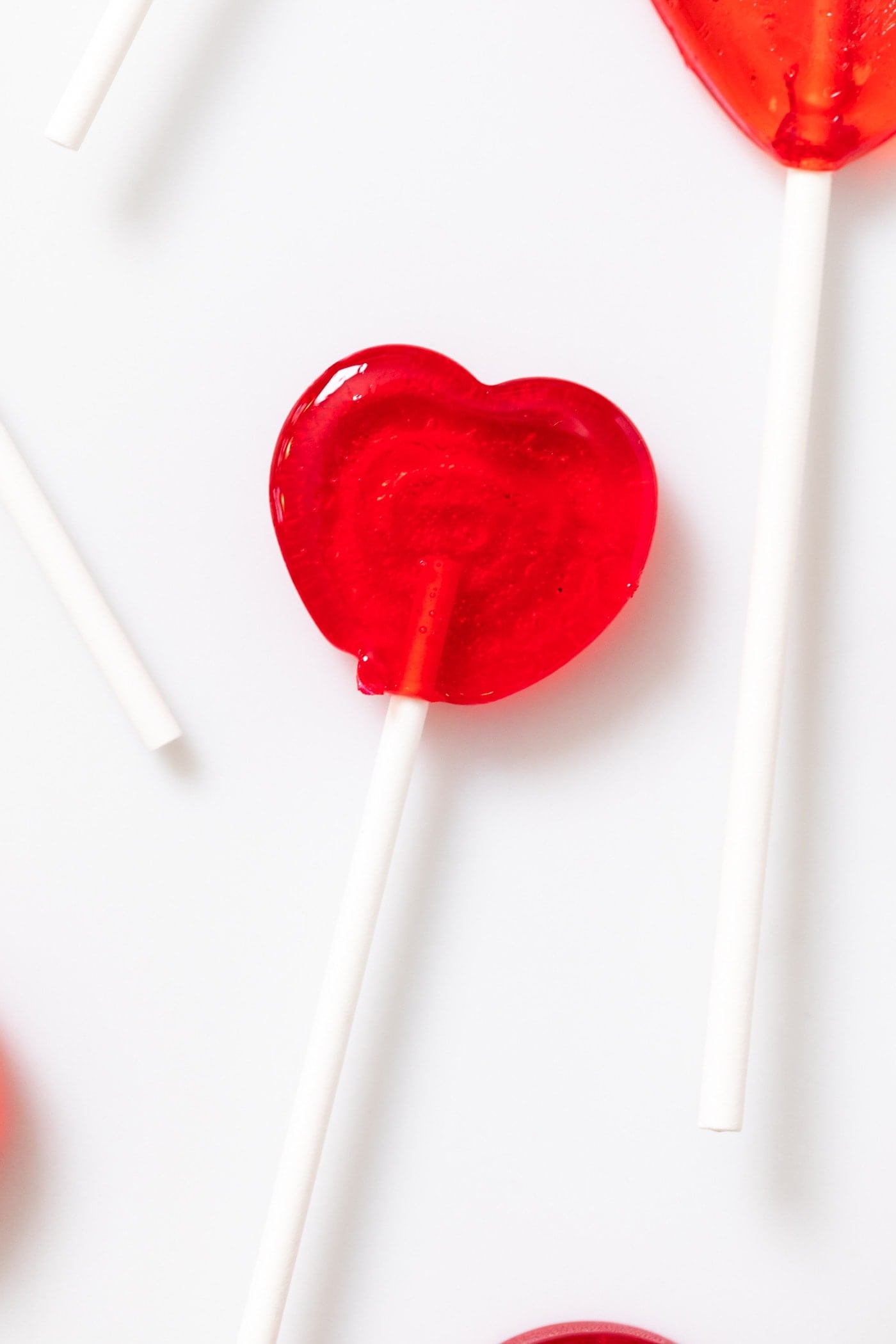 Close up view of red heart-shaped cherry sucker sitting on white countertop with sucker sticks