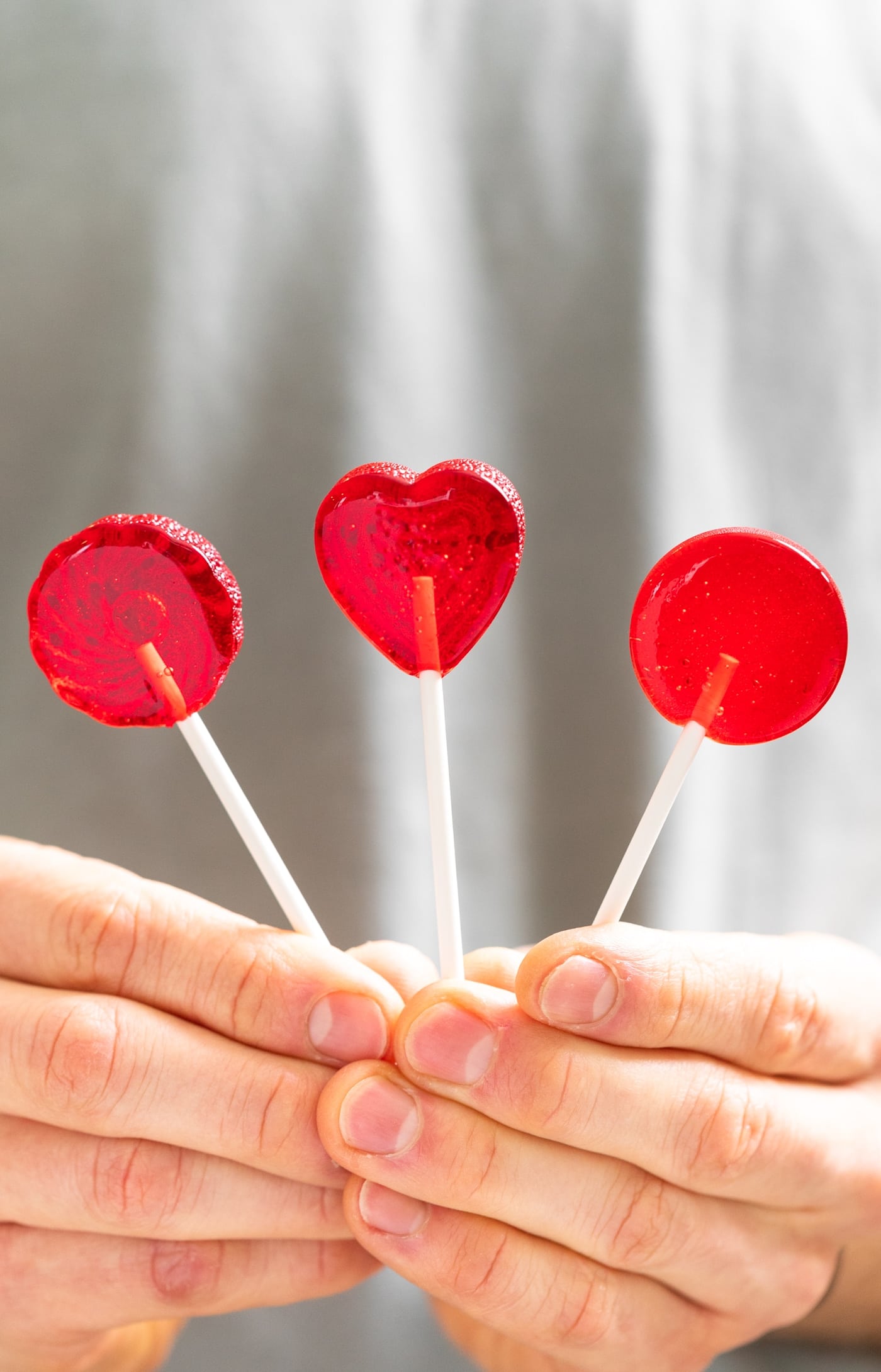 Two hands holding three circular red suckers with gray shirt in background