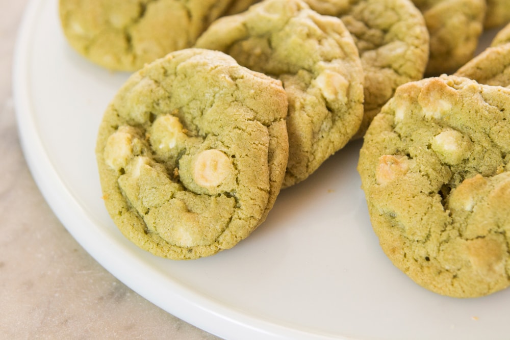 White circular serving platter with green colored matcha cookies sitting on them with white chocolate pieces