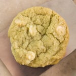 Light green colored matcha green tea cookie sitting on metal spatula on marble surface with white chocolate pieces in cookie