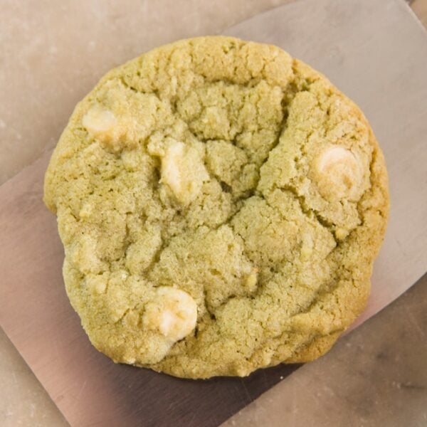 Light green colored matcha green tea cookie sitting on metal spatula on marble surface with white chocolate pieces in cookie
