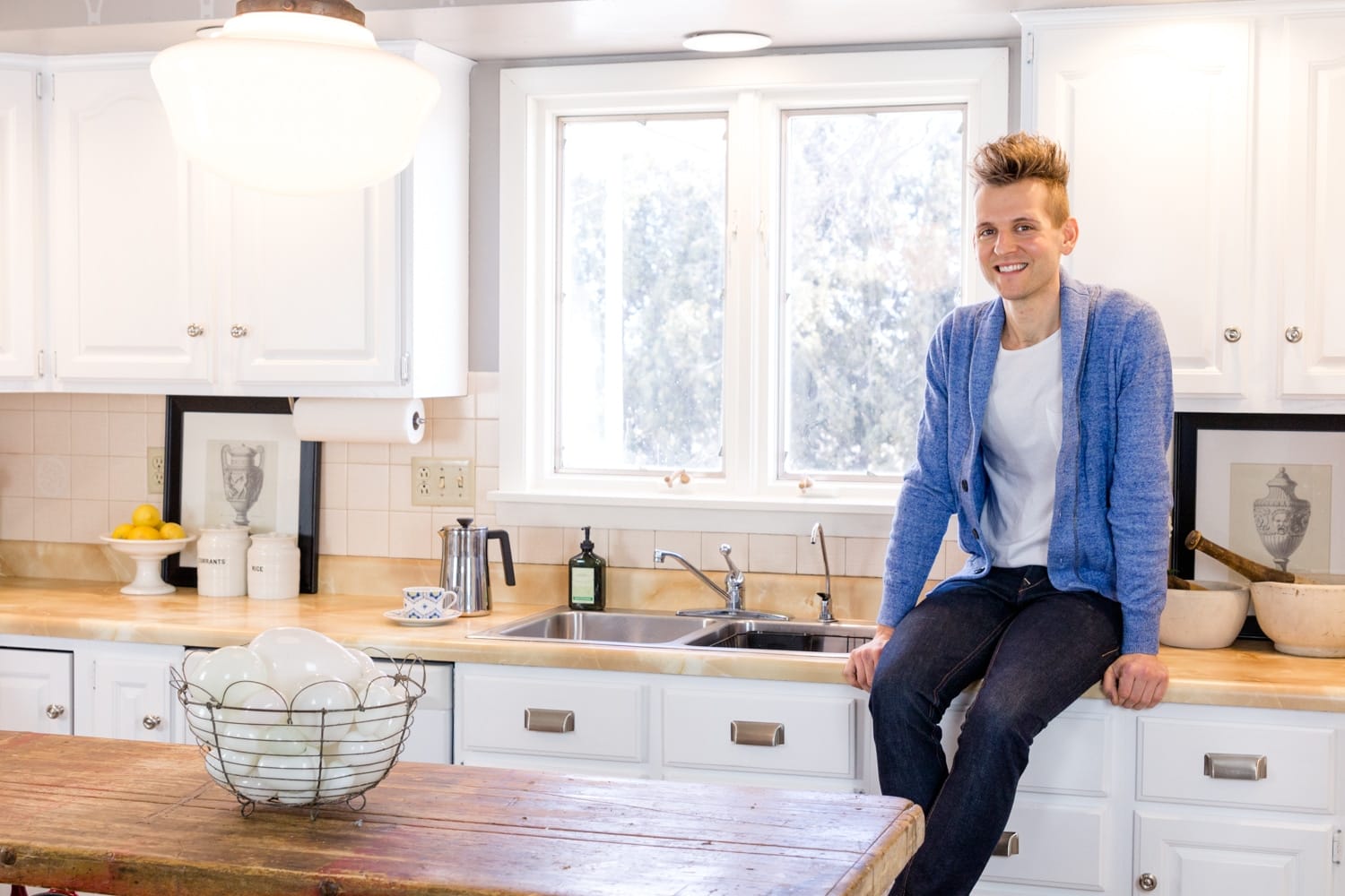 Kaleb Wyse sitting on countertop surrounded by fresh white cabinets after showing how to paint kitchen cabinets
