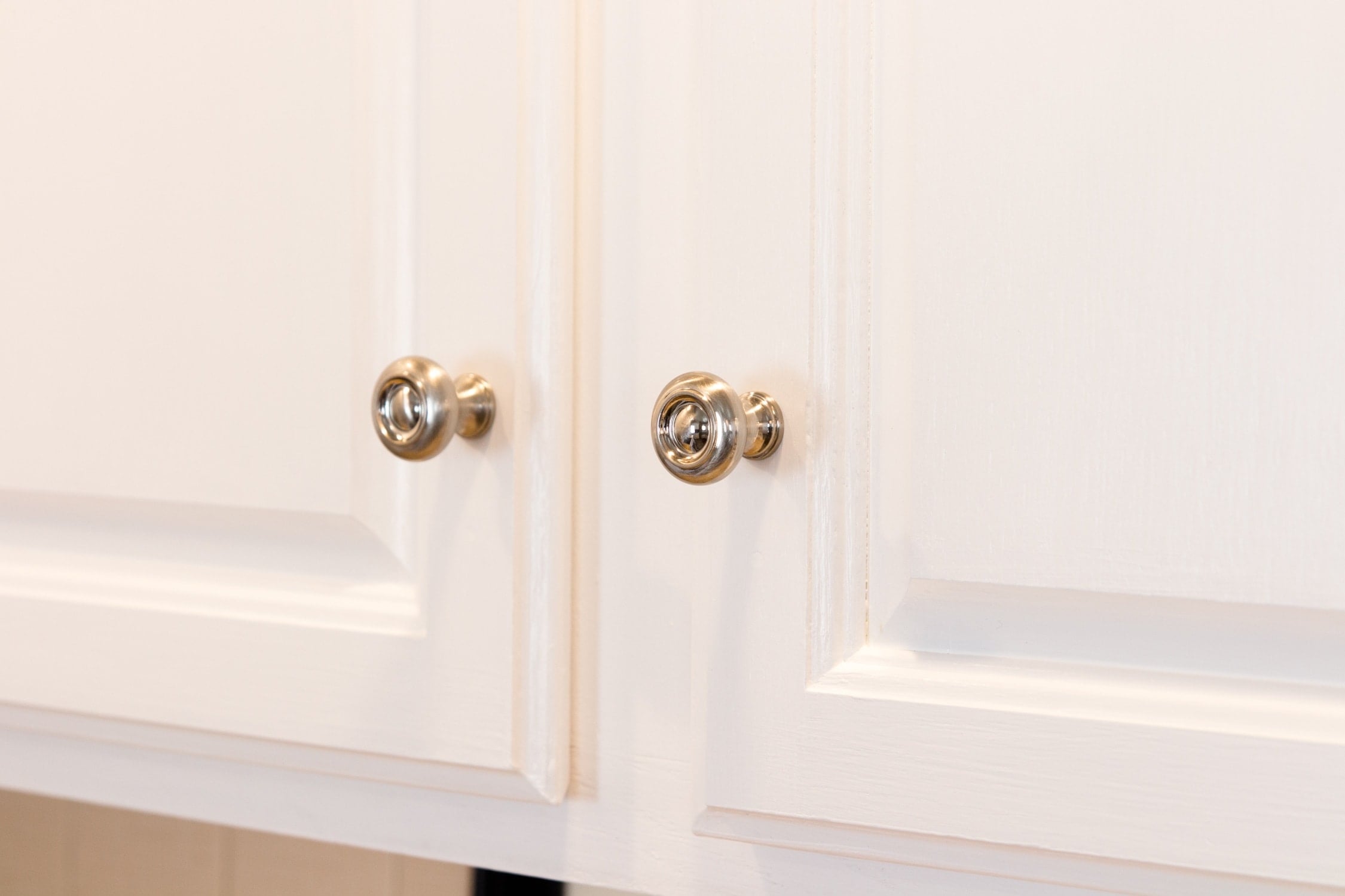 Close up view of silver pulls attached to bright white upper kitchen cabinets