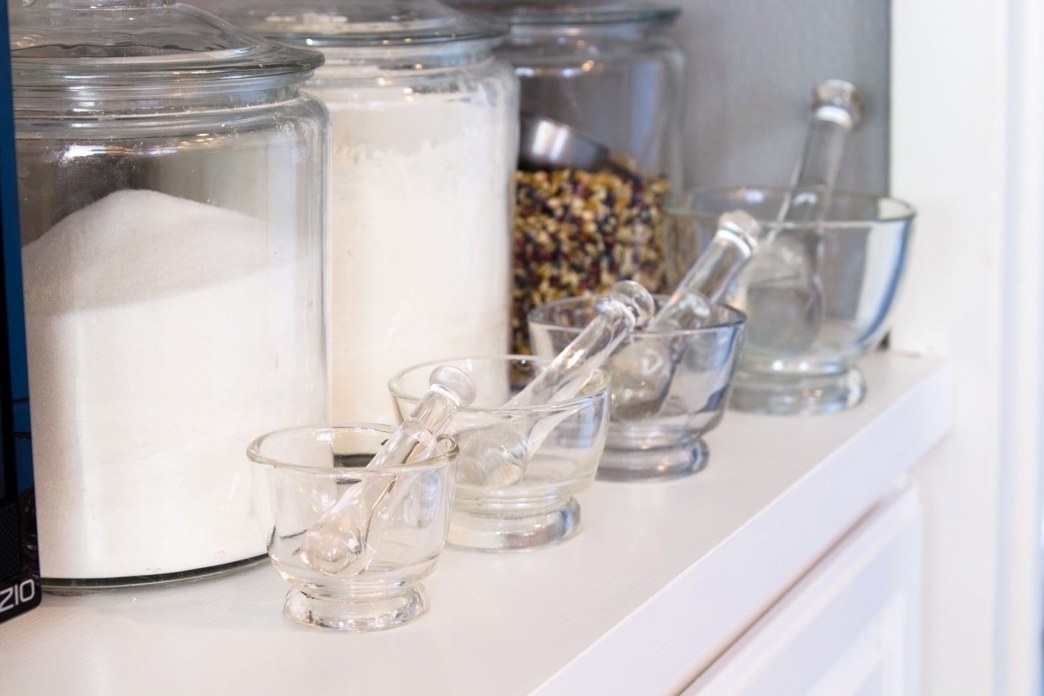 Bright white kitchen cabinets with glass kitchen containers and mortar and pestle set sitting on white countertop