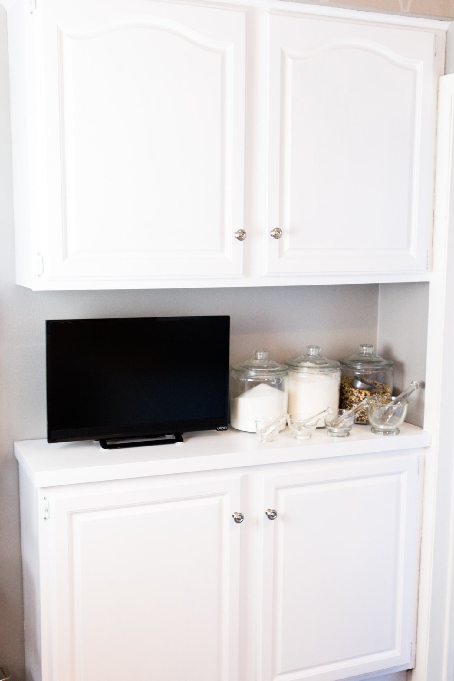 Bright white kitchen cabinets with television and jars full of kitchen supplies sitting on countertop