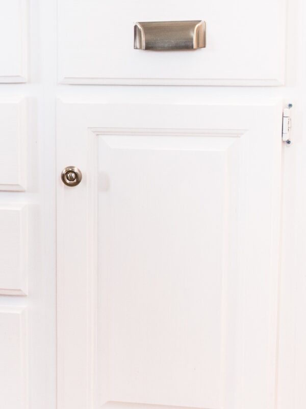 Matte silver drawer pulls attached to bright white lower kitchen cabinets