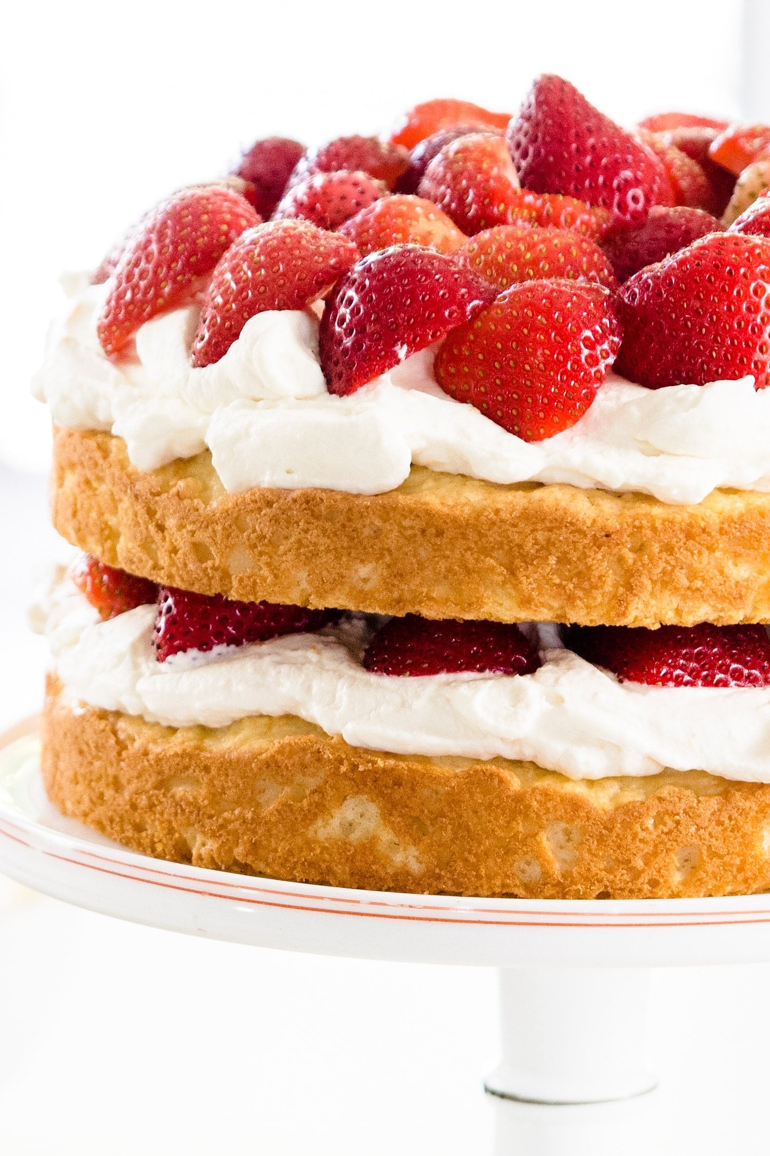 Strawberries, whipped cream and yellow cake in two layers on a white cake plate