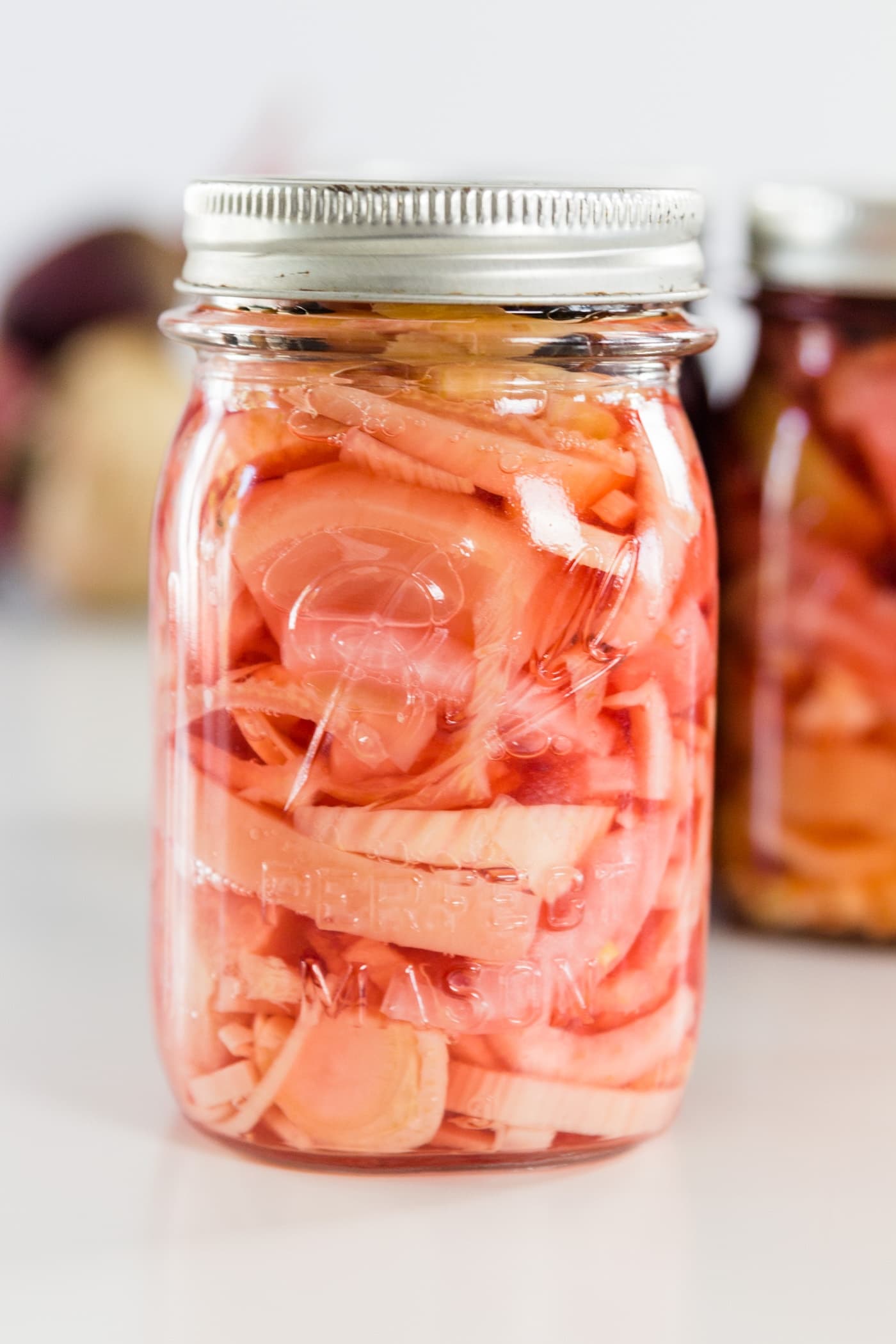 A white and pink canned beet recipe in a Ball canning jar on a white surface with Ball canning jars and beets in background.