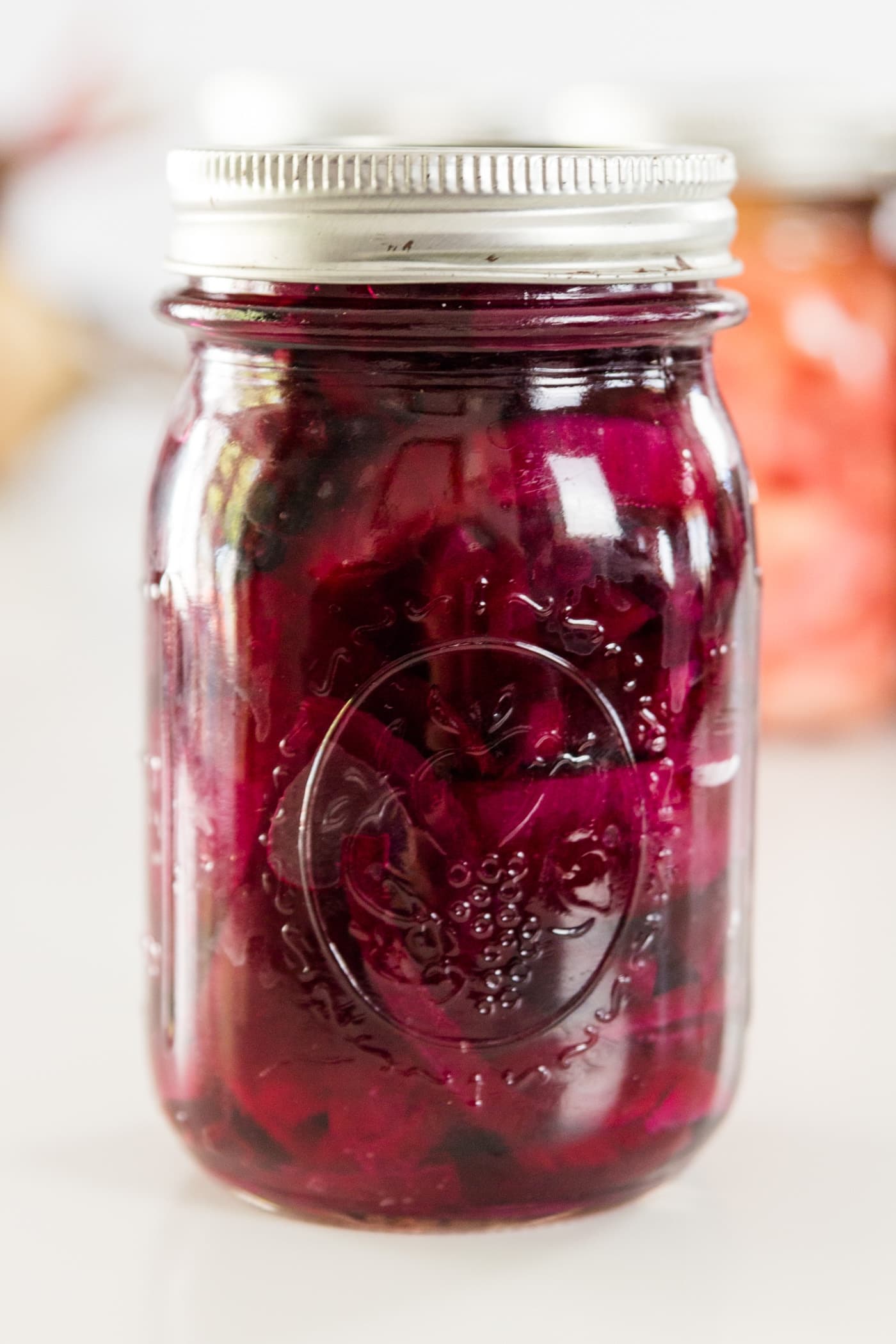A red canned beet recipe in a Ball canning jar on a white surface with Ball canning jars in background.
