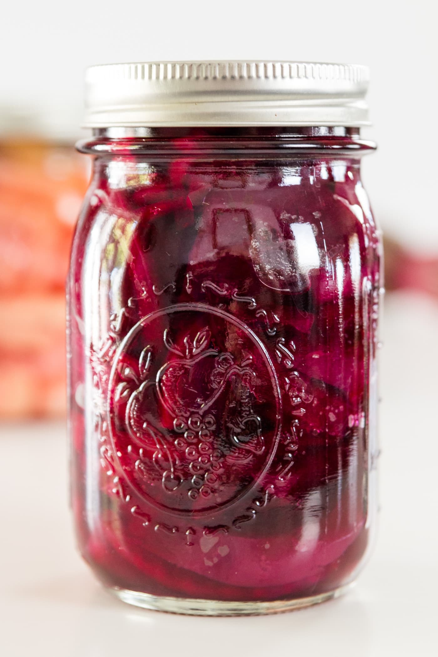 A red canned beet recipe in a Ball canning jar on a white surface with Ball canning jars in background.