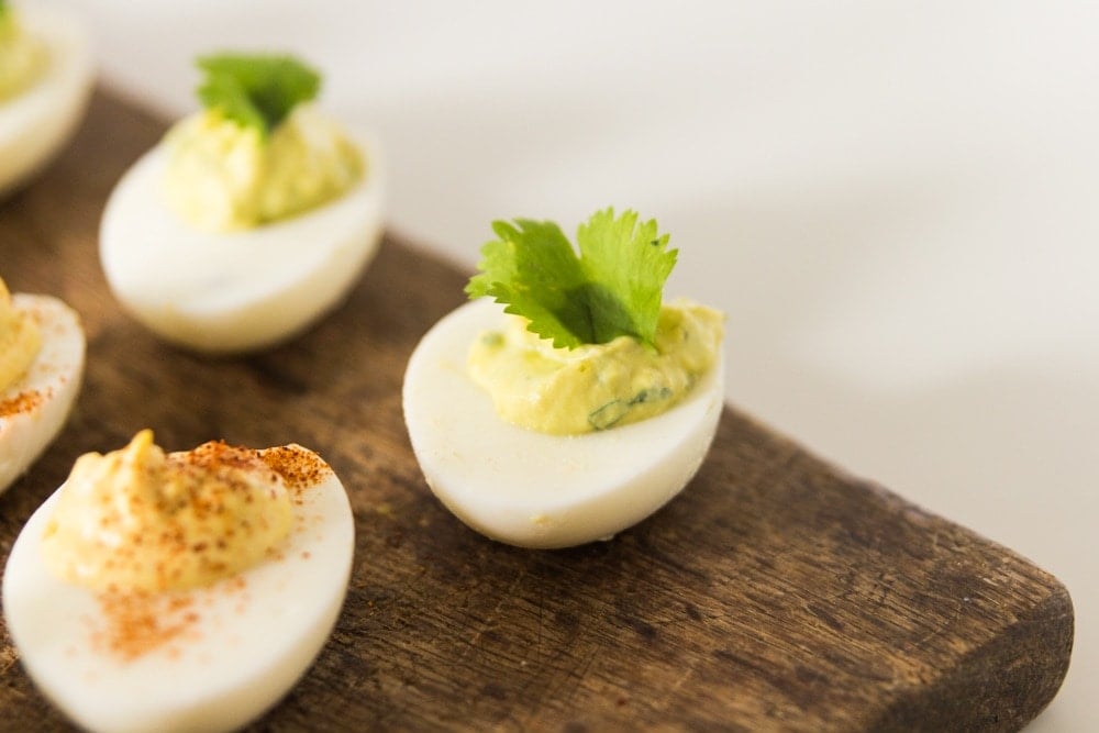 Hardboiled eggs sitting on wood board with green filling and topped with cilantro.