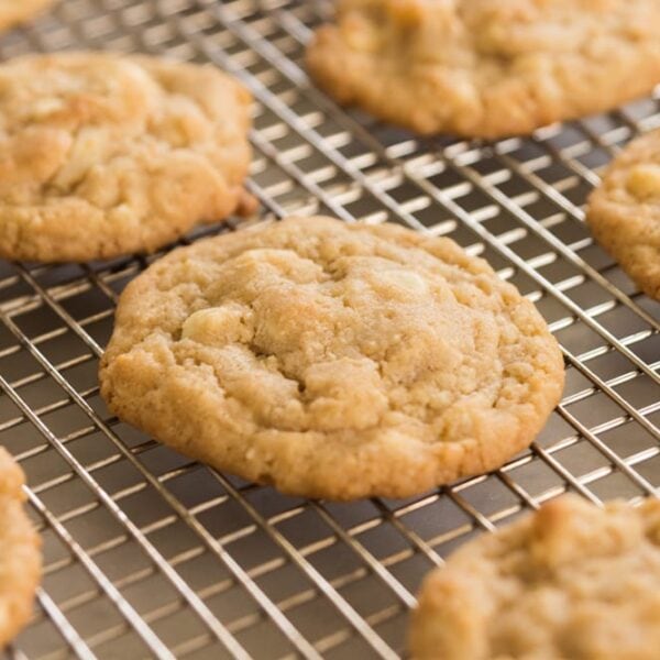 White chocolate chips showing in golden brown Macadamia nut cookies sitting on wire cooling rack with multiple cookies all around