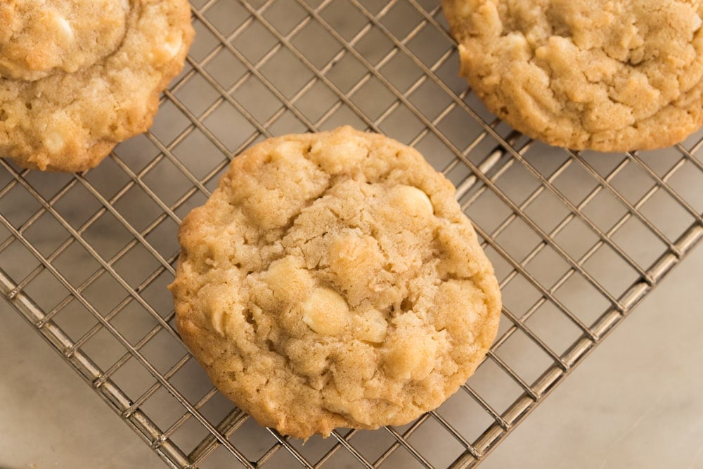 Top down view of white chocolate Macadamia nut cookie sitting on wire cooling rack on marble surface