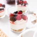 Glass container filled with triple berry cheesecake sitting on white countertop with other glasses also filled in background.