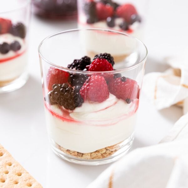 Glass container filled with triple berry cheesecake sitting on white countertop with other glasses also filled in background.