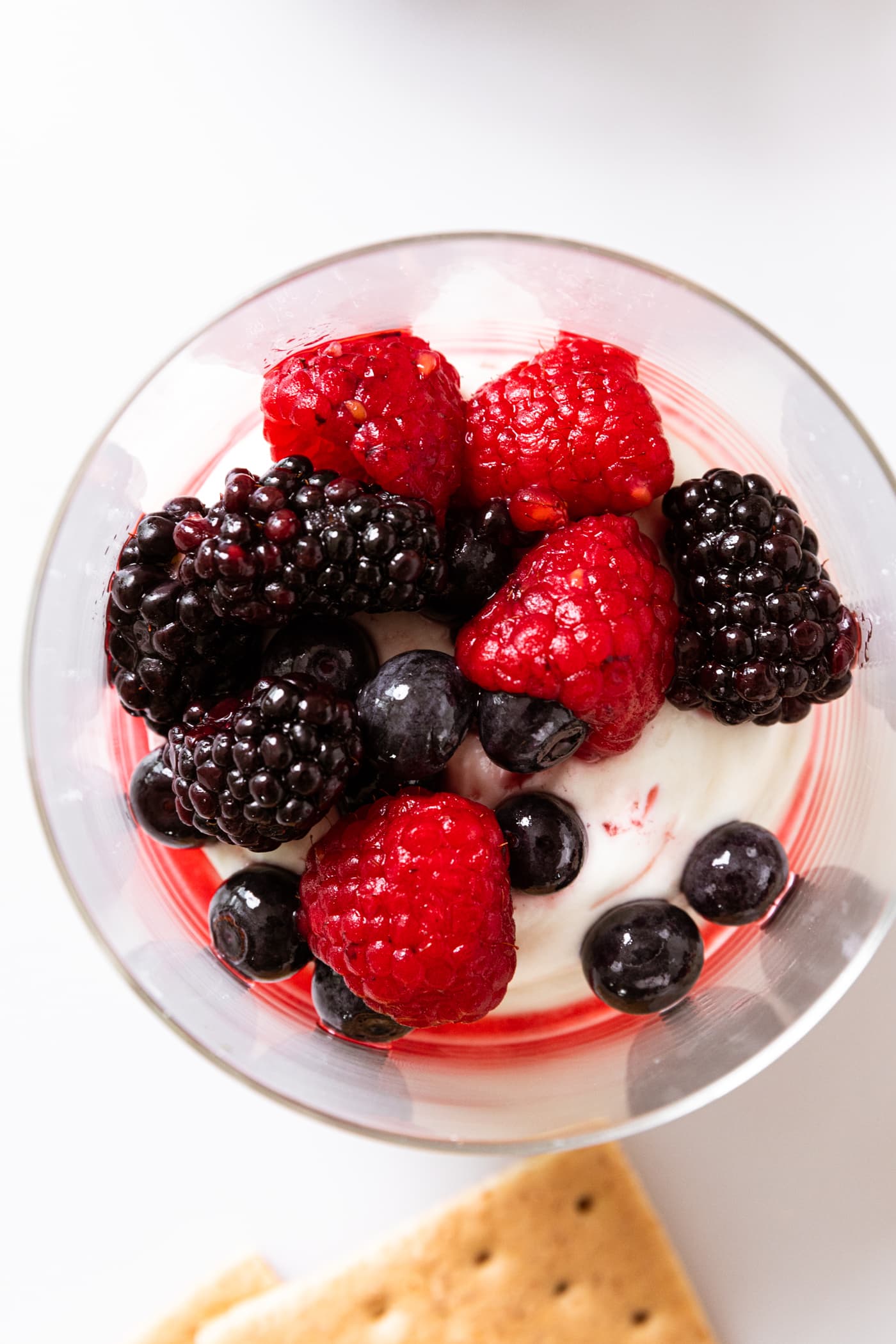 Glass filled with cream cheese and topped with a mixture of three kinds of berries sitting on white countertop.