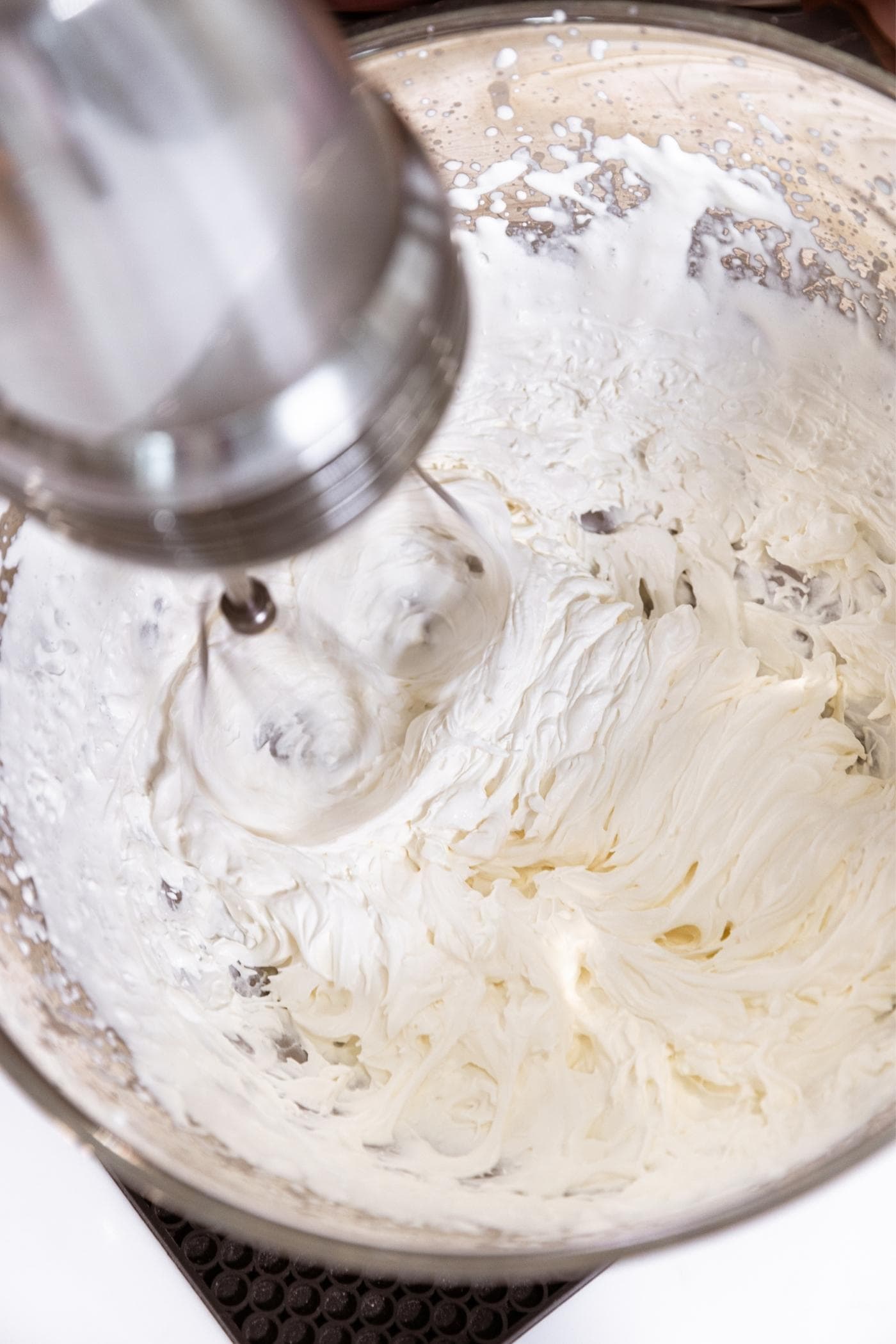 Steel mixing bowl with hand mixer spinning filled with white whipped cream.