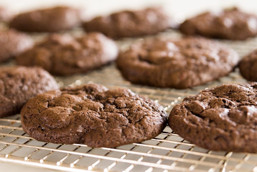 View of side of spicy dark chocolate. cookie sitting on wire cooling rack with multiple cookies in the background