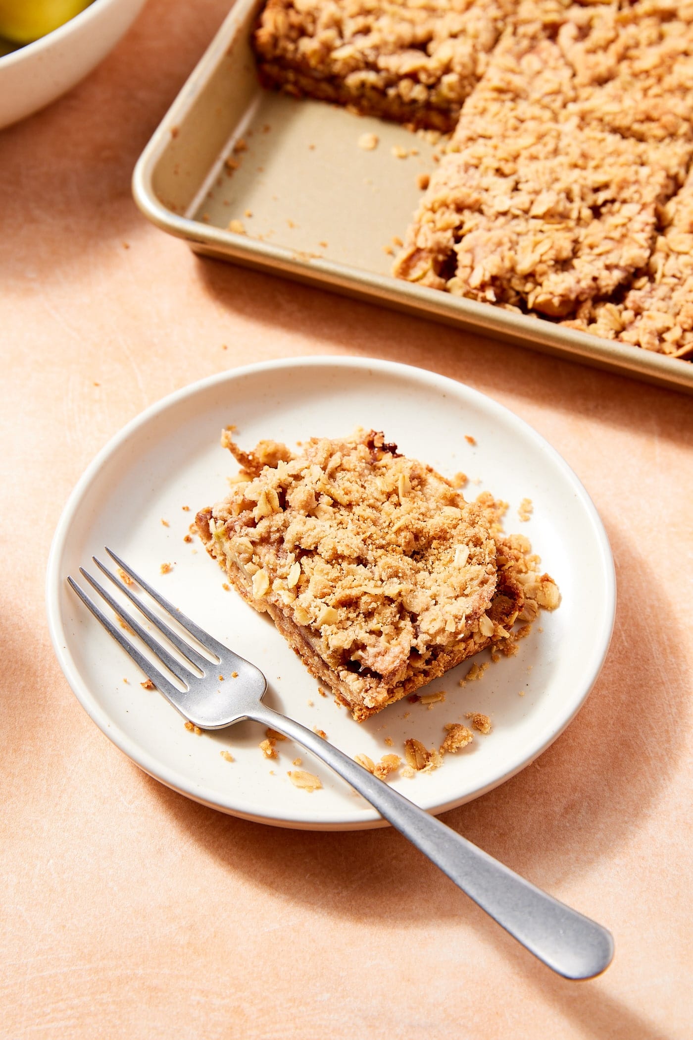 White plate with slice of apple pie bar with fork resting to the side and remaining bars in the background.