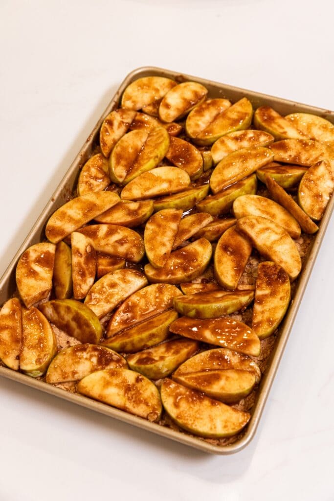 Large gold baking pan filled with baked oat crust with sliced apples all over covered in cinnamon and sugar.