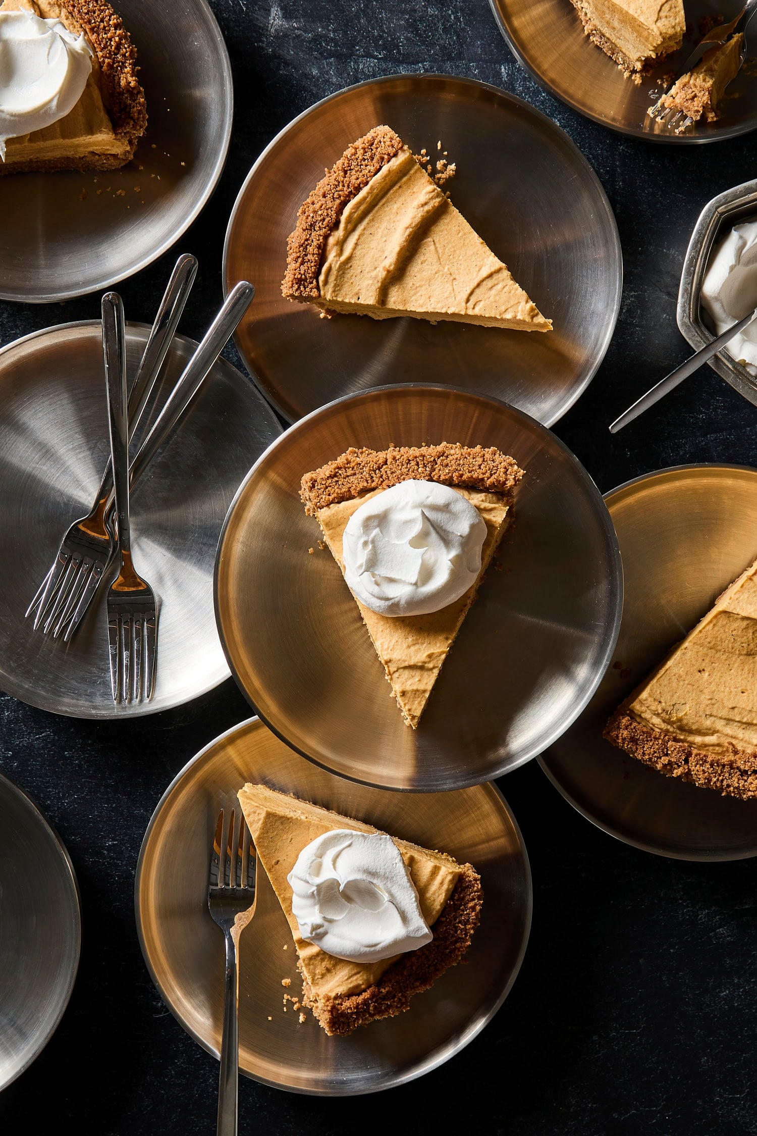 Silver plates with slices of pumpkin cheesecake topped with a dollop of whipped cream.