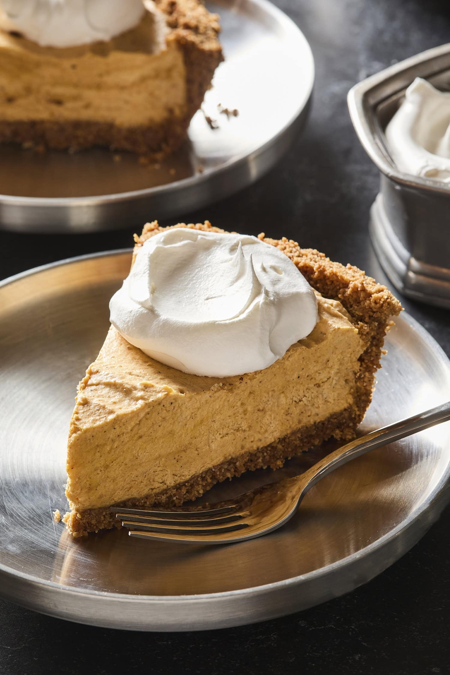 Silver plate with slice of frozen pumpkin cheesecake topped with whipped cream.