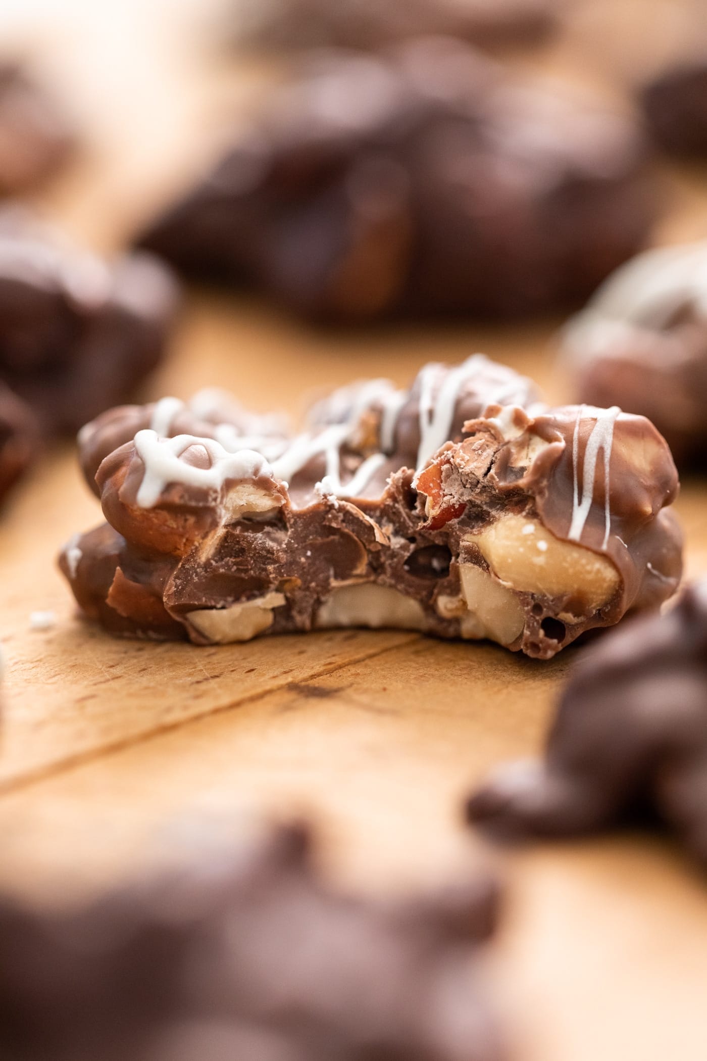 Chocolate peanut cluster with bite taken out sitting on wood surface with other chocolate clusters in background