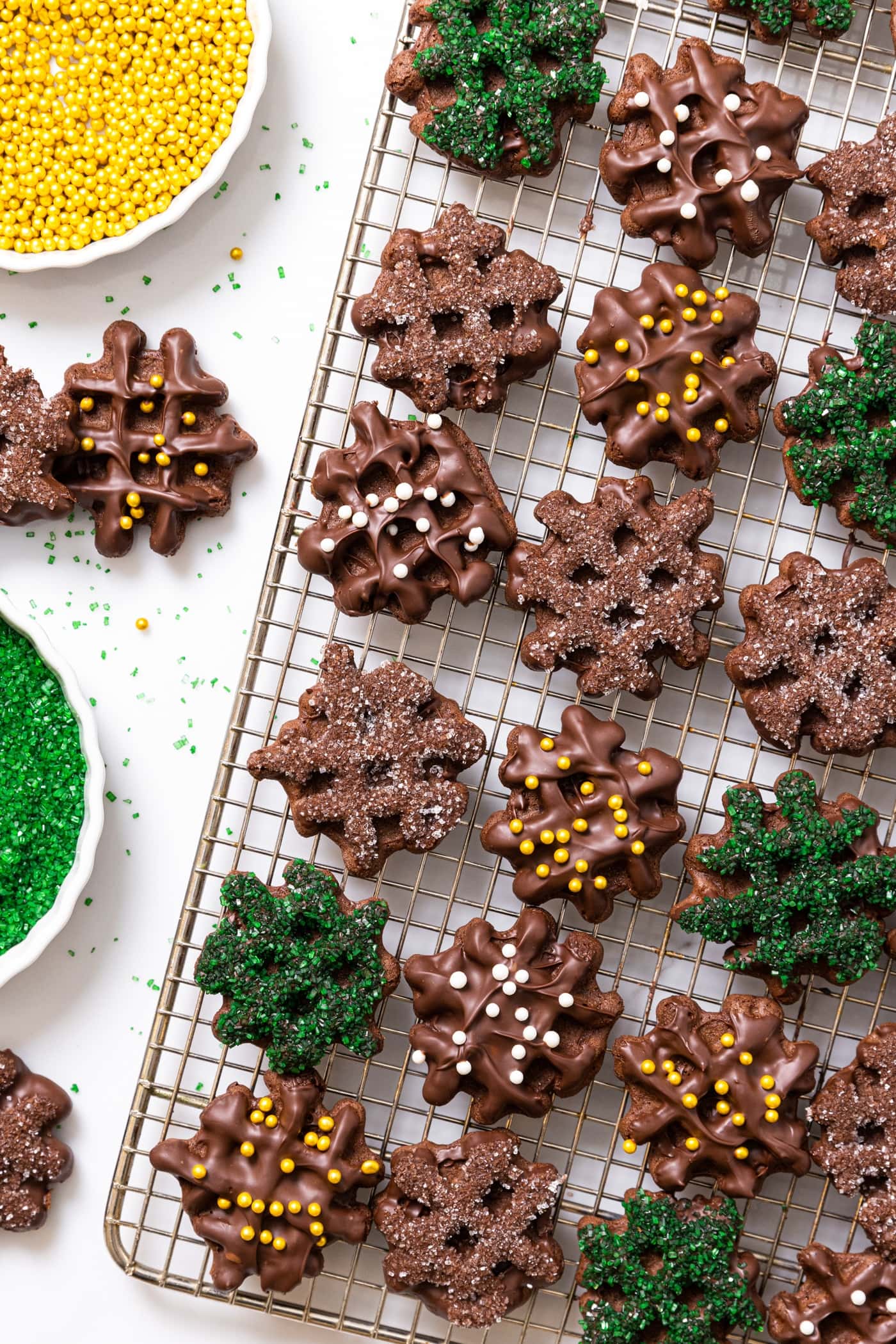 Top down view of chocolate waffle cookies sitting on cooling rack with chocolate frosting and decorations all over the top all on white countertop