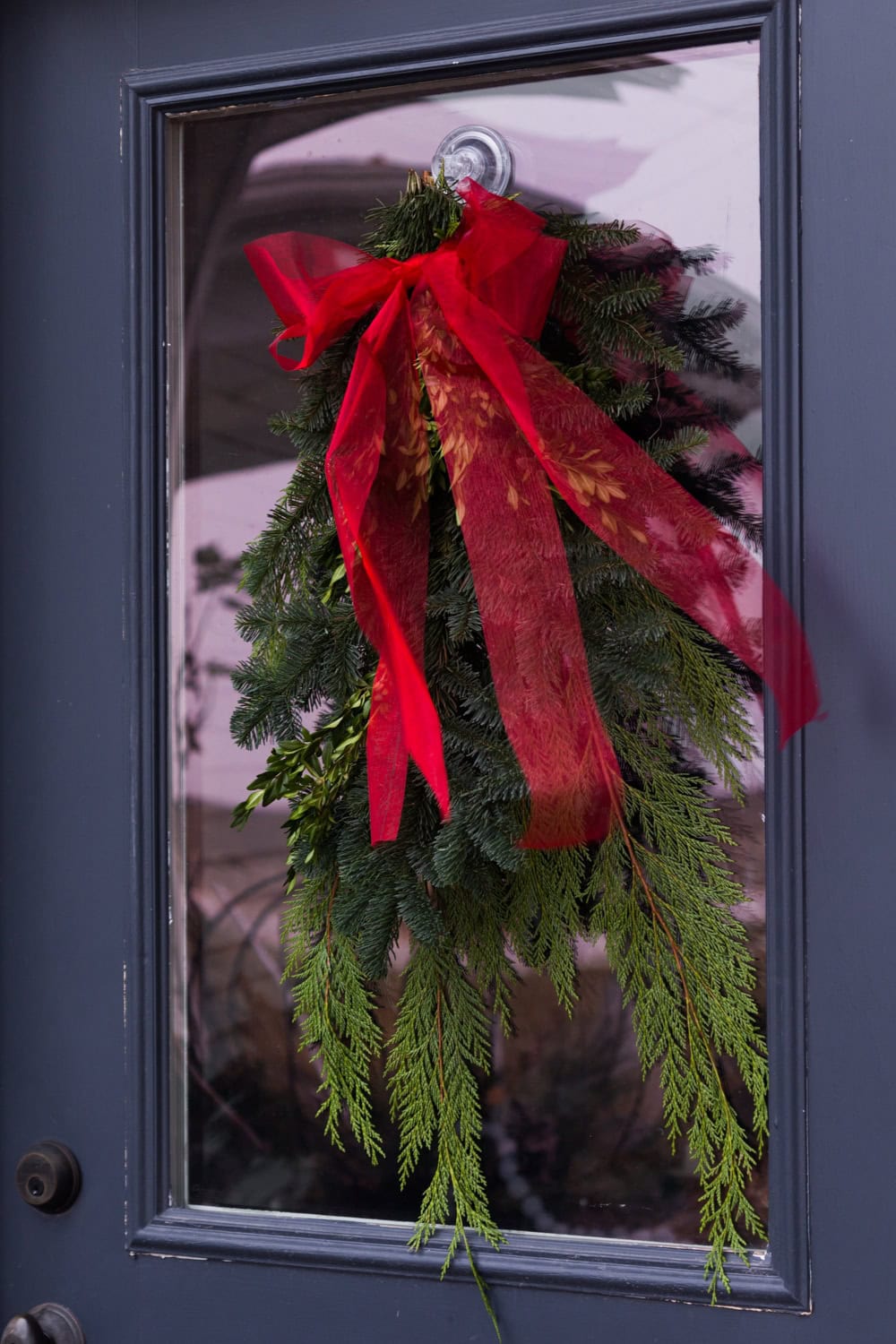 Greenery bundle attached to a front door with a wispy red ribbon adorning the top.