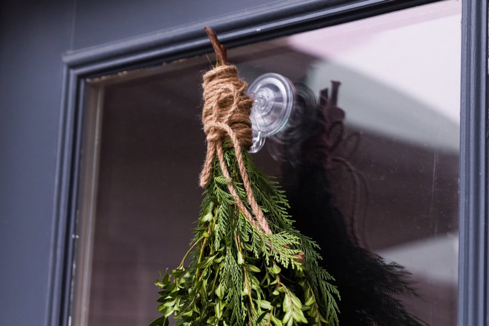 Twine used to tie up a holiday evergreen bundle attached to the window of a door with a suction cup.