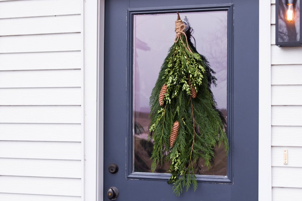 A greenery filled holiday swag attached to a blue door for the holiday season tied together with twine.