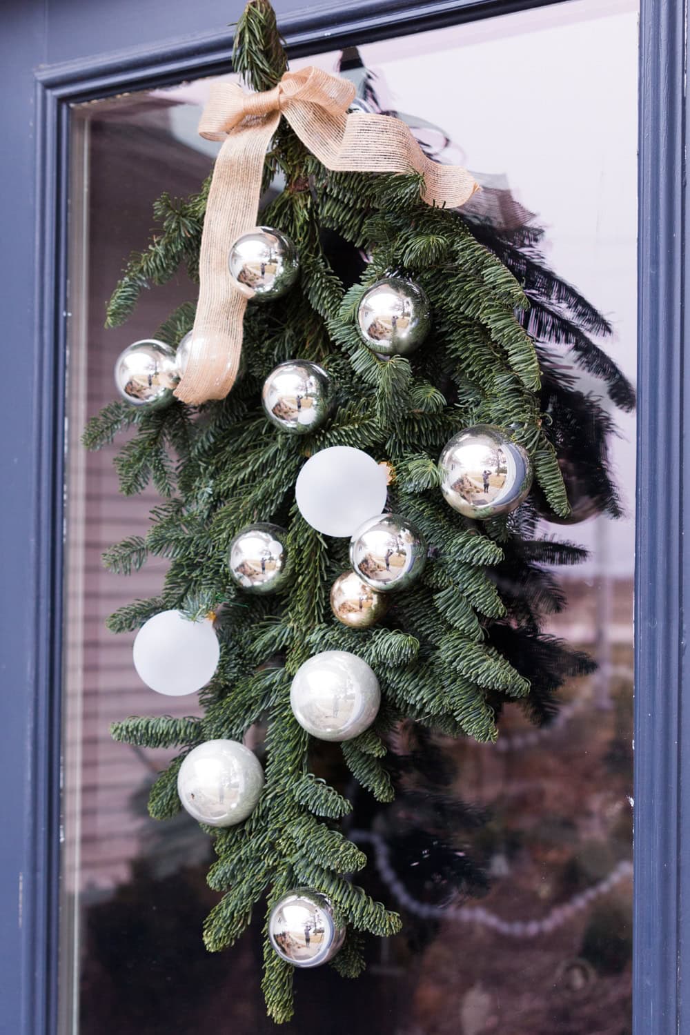 An evergreen holiday swag adorned with silver balls hanging on a blue door.