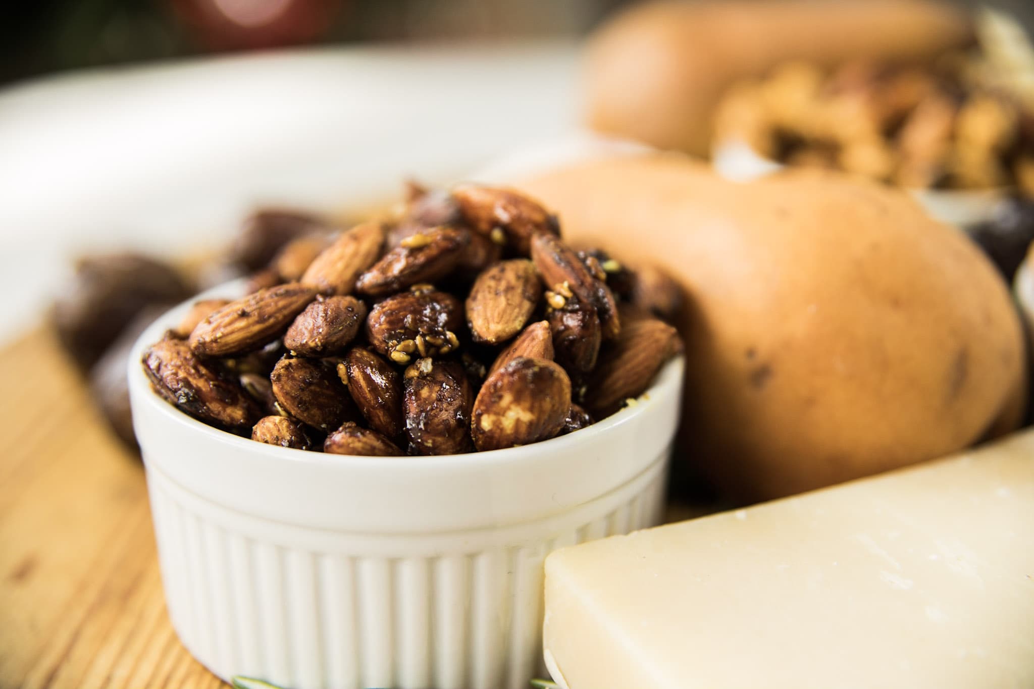 White bowl filled with toasted almonds with pear and hunk of cheese around all on wooden board