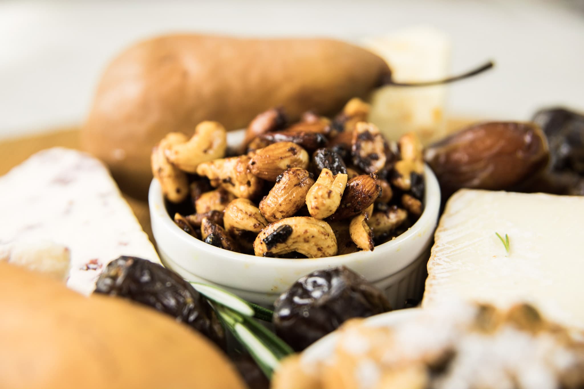 White bowl filled with mixed nuts with pears, dates, and cheese all around on white surface