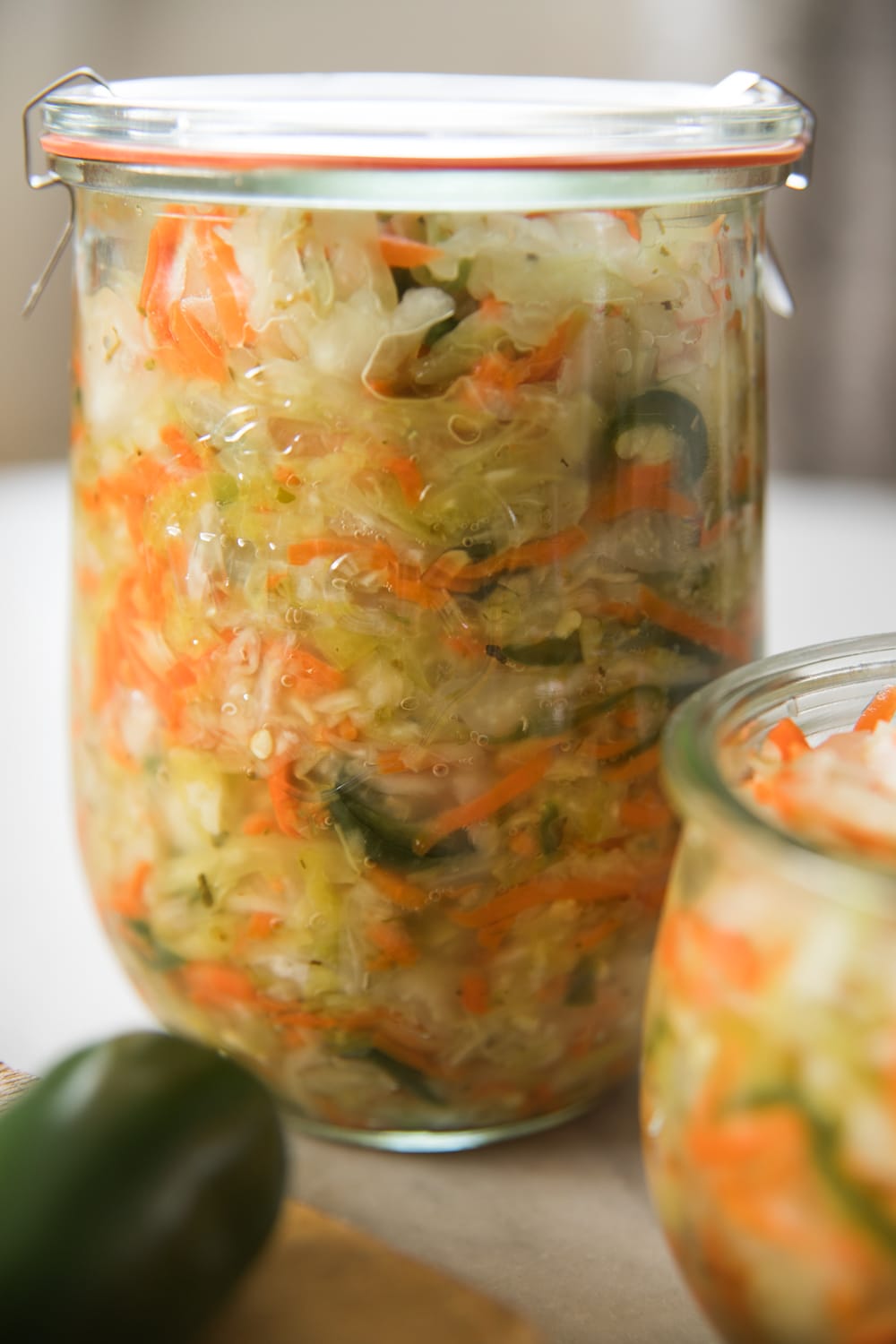 Large glass jar filled with curtido relish made from slices of cabbage and carrots and bits of jalapeño with liquid poured on top