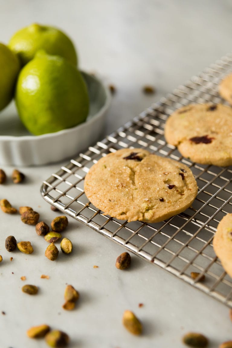 Flat shortbread cookie sitting on wire cooling rack with limes in background all on marble surface