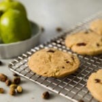 Shortbread cookie sitting on cooling rack with pistachios all around with limes in background